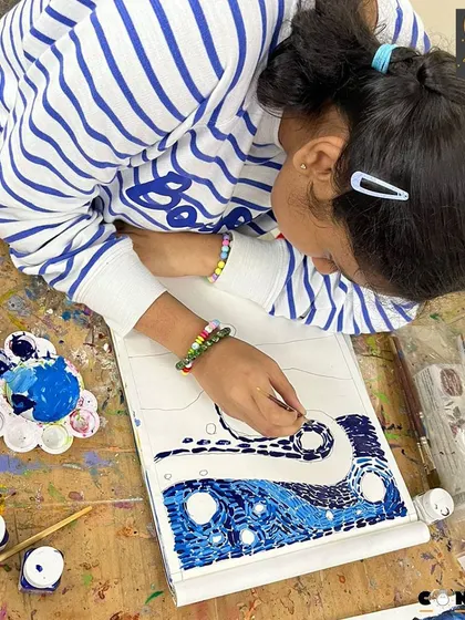 A young artist carefully applies dabs of paint to her 'Starry Night' inspired artwork, showing great focus and patience.