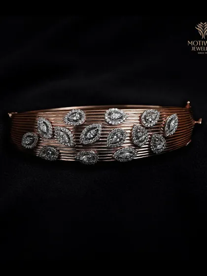 A wide cuff bracelet in rose gold, adorned with marquise-shaped diamond settings. The textured, linear pattern of the cuff adds a modern, sophisticated touch.