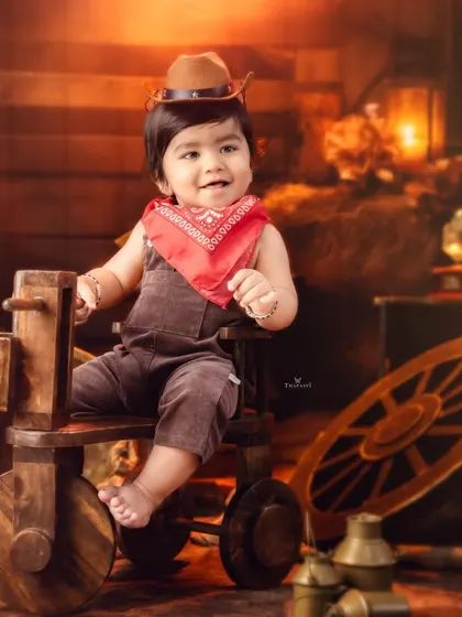 Another little cowboy ready for the rodeo, dressed in a brown hat and red bandana in a warm, rustic setting.