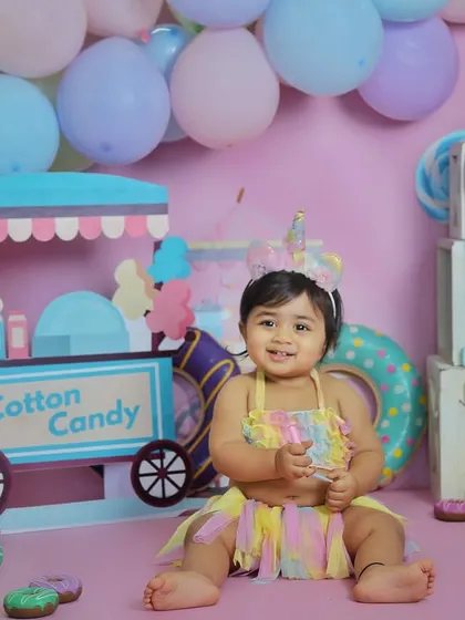 A happy one-year-old in her colorful candyland setup. The unicorn headband and pastel dress complete this adorable first birthday look.
