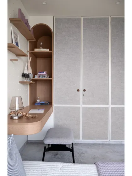 This view shows the study area next to the fabric-paneled wardrobes. The arched shelving and curved desk create a soft, inviting workspace that is seamlessly integrated into the room's design.