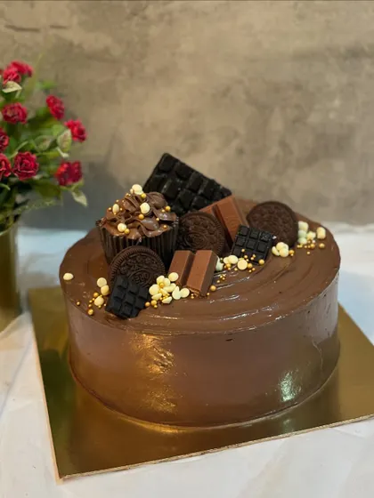 A chocolate cake topped with a variety of treats including Oreos, KitKats, and a chocolate cupcake.