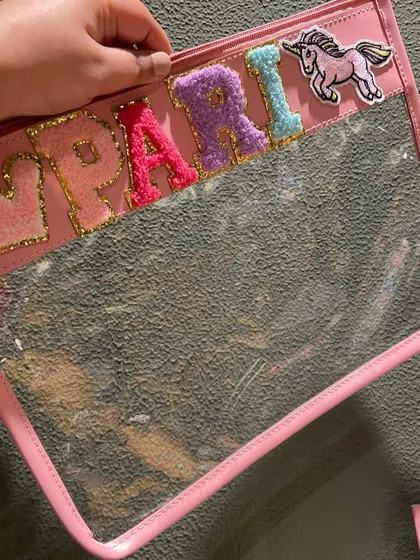 This clear travel pouch with a pink border is personalised with a name and a unicorn patch, making it a magical accessory.