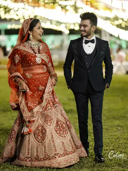 A full-length shot of a couple in their wedding attire, sharing a laugh in a garden setting at night.