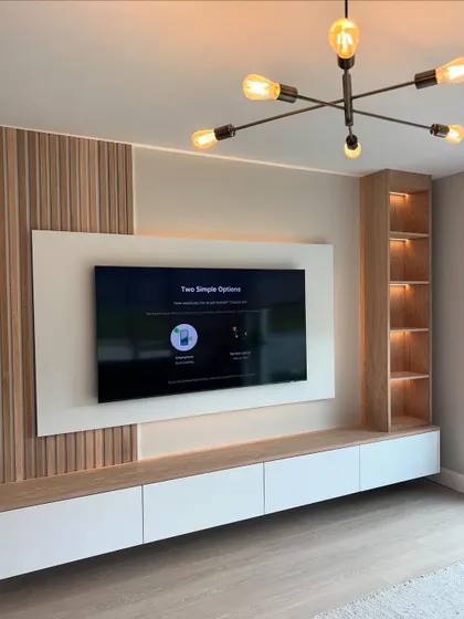 This TV unit design balances different textures beautifully. It features light wood fluted panels on one side, a built-in display shelf on the other, and a clean white floating console, all tied together with warm backlighting.