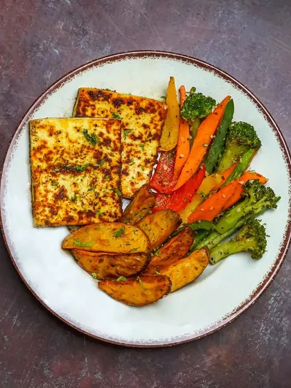 A vegetarian platter featuring grilled paneer steaks, seasoned potato wedges, and colorful sautéed vegetables.