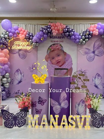 A full view of a butterfly themed first birthday party, complete with a custom photo backdrop, balloon arch, and 'BABY' blocks.