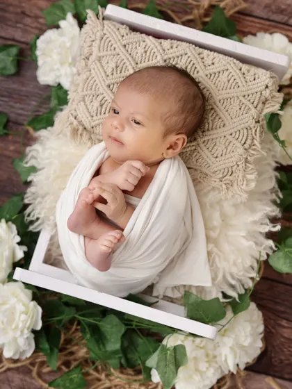 An awake and curious newborn, swaddled in white, looks up from a cozy bed of fur and flowers. Capturing these moments of quiet alertness is just as special as the sleepy ones.