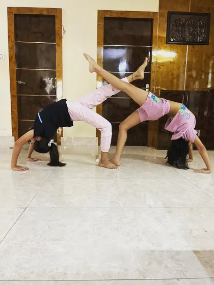 Two students perform a synchronized backbend with leg extensions, a beautiful display of teamwork and flexibility.