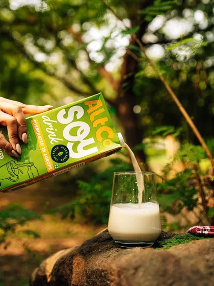A refreshing pour shot of Alt Co.'s soy milk into a glass, set in a natural, outdoor environment. The greenery in the background enhances the product's connection to nature.