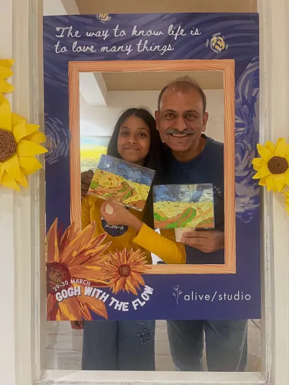 A father and daughter posing at our Van Gogh-themed photo booth after finishing their wheat field paintings.