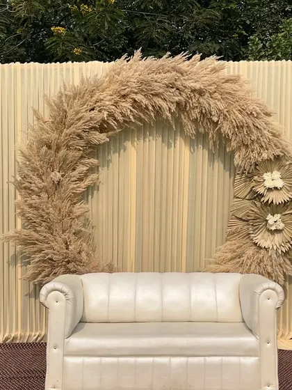 A chic and minimalist backdrop for an engagement or reception. The design features a large arch made of dried pampas grass against a simple cream-colored drape.