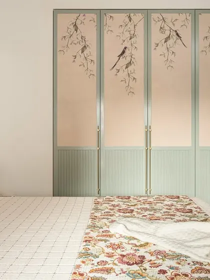 The wardrobe in the 'Palaash' master bedroom is a delight, featuring a soft sage green finish and beautiful wallpaper with a bird motif. It's a perfect example of our attention to artistic detail.