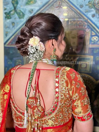 A full view of the bride in her red and gold saree, with her hair in a traditional floral bun. This shows how the hairstyle complements a classic South Indian or Bengali bridal look.