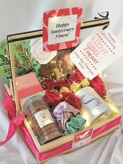 A romantic anniversary hamper curated with love. This gift includes a personalized mug, cookies, a photo frame, skincare, and satin scrunchies, all arranged with fresh roses and fairy lights.