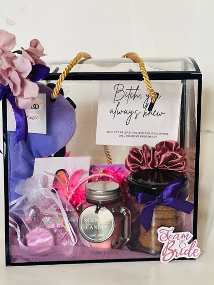 This bridesmaid hamper is filled with goodies like scrunchies, cookies, a candle, and chocolates. The personalized card makes the proposal feel extra special.
