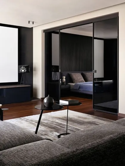 The upper floor of Villa Aish was conceived as a private studio apartment. This view shows the living area transitioning into the bedroom through smoked glass sliding doors, creating a sophisticated and moody suite with a darker, more intimate material palette.