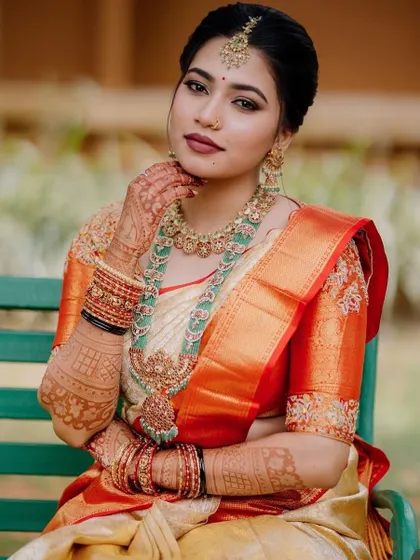 The complete bridal look. The rich orange blouse with intricate sleeve embroidery stands out beautifully against her traditional South Indian wedding saree.