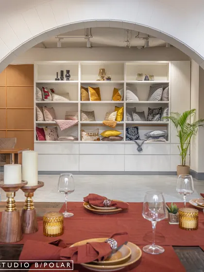 The deep red table setting in the foreground provides a rich pop of color against the neutral tones of the store. In the background, the well-lit shelving unit acts as a library of textiles, showcasing the range of colors and patterns available.