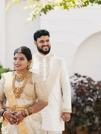 A candid shot of the couple in their white and gold wedding outfits, walking together in a sunlit garden.