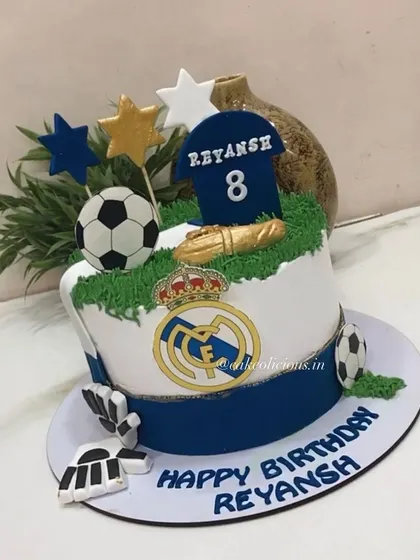 A Real Madrid themed football cake for an 8th birthday. This cake is perfect for a young sports fan, featuring the team logo, a football, and a jersey topper.