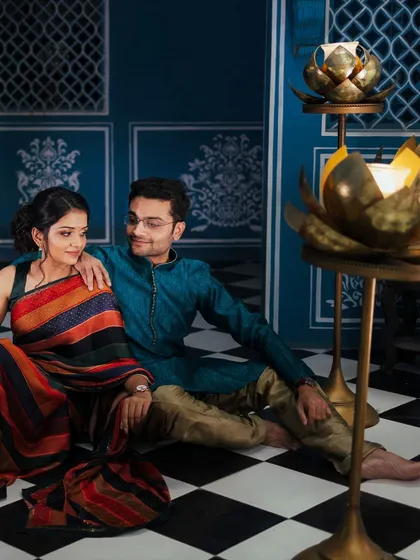 An intimate moment from a styled shoot, with the couple seated amidst brass lotus candle holders. The warm lighting and traditional decor create a rich and romantic atmosphere for this pre-wedding portrait.