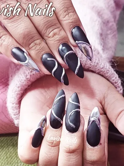A striking and unique design featuring long, stiletto-shaped nails. The matte black base is contrasted with raised, 3D silver chrome swirls and accents, creating a futuristic and textural look that is both dark and glamorous.