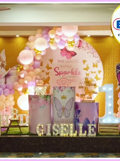 A beautiful butterfly and fairy-themed first birthday. The pink and purple decor features a 'She leaves a little sparkle' backdrop, a 'GISELLE' marquee, and a large light-up number '1'.