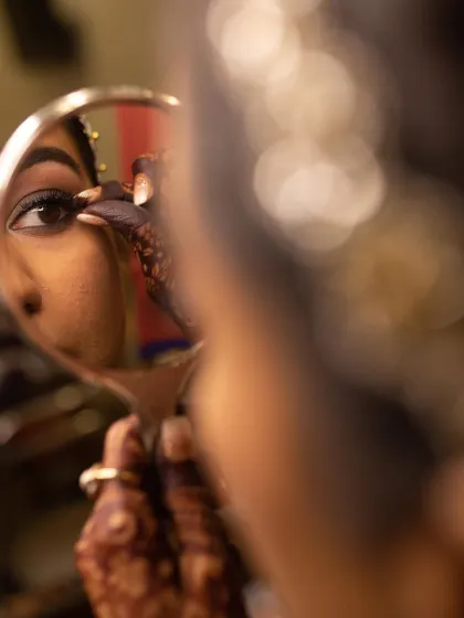 An artistic reflection shot. You can see the bride's intricate henna as she holds a mirror for her final makeup touches, a beautiful detail from her wedding day.