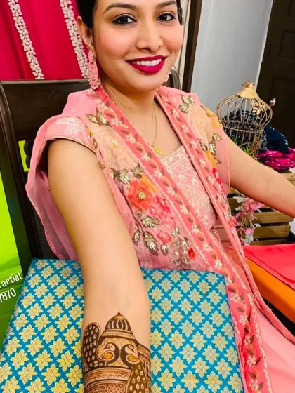 A smiling bride during her mehndi application, with a close-up on the beautiful peacock design taking shape on her arm.