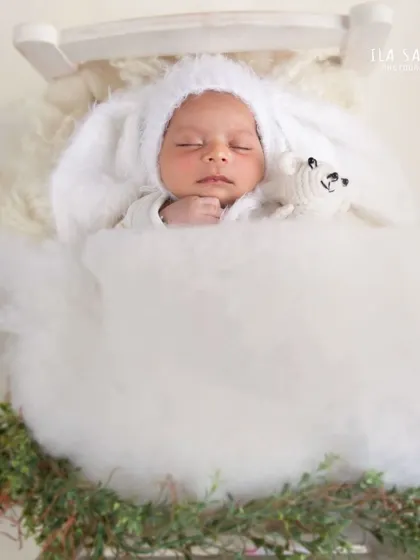 A dreamy newborn portrait. This baby is sleeping peacefully in a tiny bed, dressed in a fluffy bunny bonnet, creating a whimsical and adorable scene.