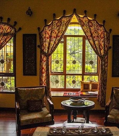 This cozy seating area in the Roopa Hariprasad Residence features a bay window with custom traditional drapery. The space is designed to be a comfortable nook for reading and conversation, filled with warm light and rich textiles.