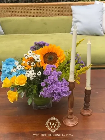 A vibrant floral backdrop and welcome sign for a colorful Haldi and Mehendi ceremony. The mix of orange, blue, purple, and yellow flowers created a stunning photo opportunity for the couple and their guests.