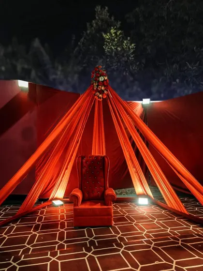 A dramatic photo corner with a single, throne-like red chair under a canopy of red drapes. The uplighting and patterned floor add to the theatrical and luxurious feel of this setup.