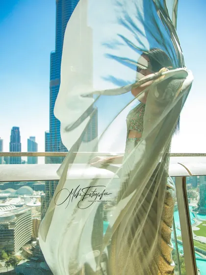 An artistic shot using the sheer fabric to partially obscure the model, creating an ethereal and mysterious effect. The Dubai skyline in the background grounds the image in a modern, luxurious setting.