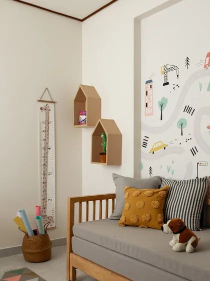 This kids' room follows a neutral color theme, with a playful road-map wallpaper adding a touch of fun. A daybed with colorful cushions, house-shaped shelves, and a growth chart make the space feel personal and ready for play.