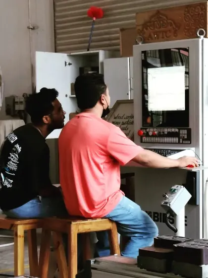 Two students collaborate at the CNC control station, learning to program and troubleshoot complex cutting paths for their projects.