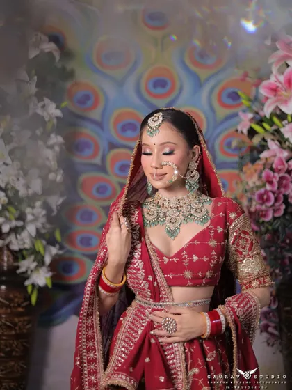 A serene portrait of the bride with her eyes closed, showcasing her stunning makeup and heavy bridal jewellery. The peacock feather background adds a touch of traditional artistry to the photograph.