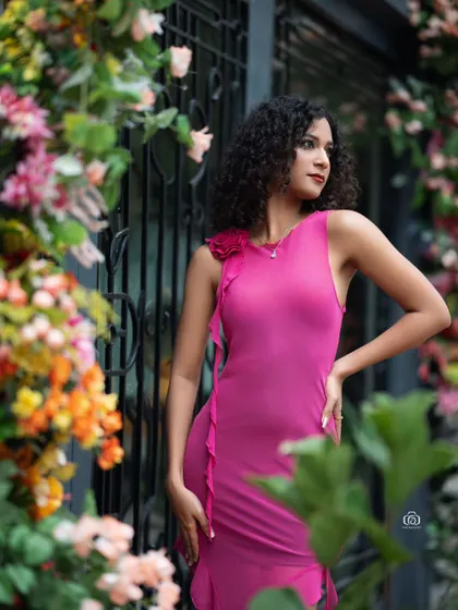 A portrait of the model in a pink dress, looking off to the side. The out-of-focus flowers in the foreground and background create a beautiful sense of depth.