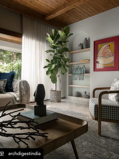 A close-up of the coffee table styling, with a sculptural black object, books, and decorative branches. The checkered armchair and Jamini Roy painting are visible in the background.