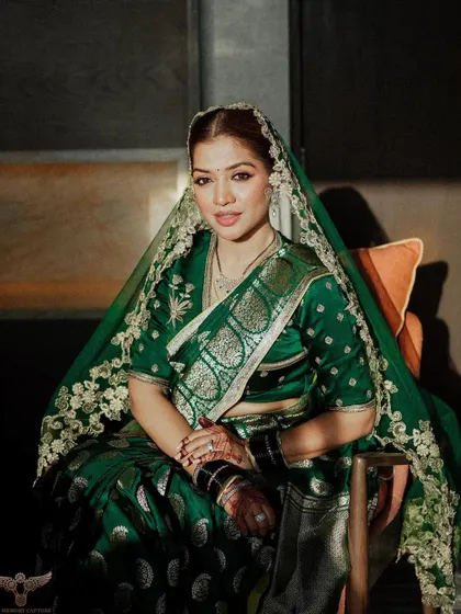 A classic, seated portrait of a bride in a stunning emerald green saree. The soft, directional light highlights the rich fabric and her serene expression.
