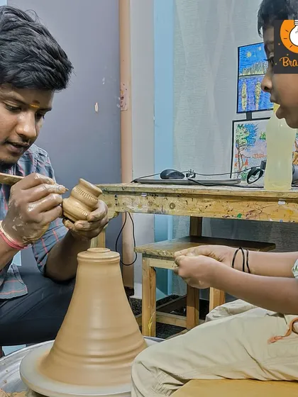 An instructor helps a young boy add details to his pot, providing the guidance needed to create a finished piece.