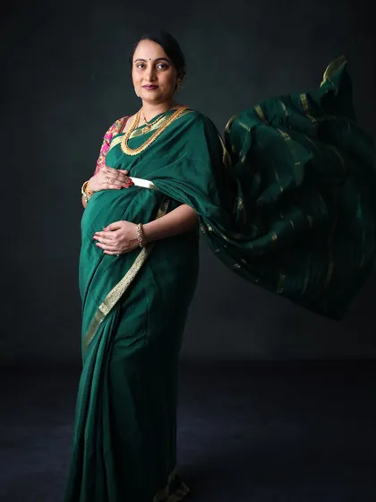 A graceful portrait of a mother-to-be in a deep green saree. The flowing fabric and classic studio lighting create a timeless and sophisticated look.