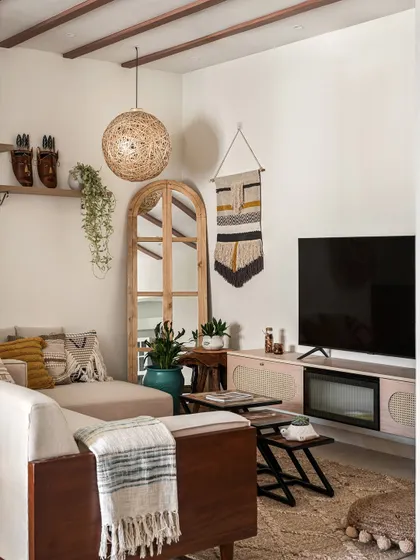 A cozy, bohemian-inspired living room with a low-profile sofa, layered rugs, and natural decor elements like a rattan pendant light and a large arched mirror.