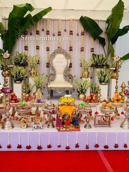 A classic and auspicious Seemantha setup featuring banana leaf pillars and cow figurines. The 21-plate arrangement is meticulously organized on a white-clothed table, ready for the ceremony.