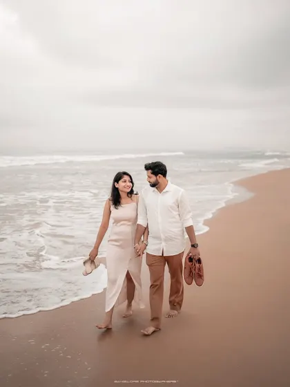 A full-length shot of a couple walking by the water's edge, capturing the peaceful and romantic atmosphere of a beach pre-wedding session. Their relaxed posture and connection tell a story of comfortable love.