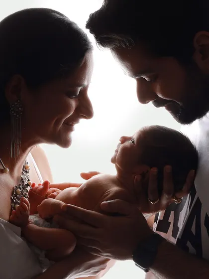 An unswaddled baby held securely in their parents' hands. This silhouette shot is powerful because it shows the baby's natural form and the parents' gentle, protective hold.