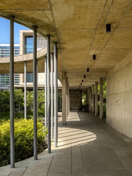 A shaded walkway at the JSW Vasind campus, where the interplay of light and shadow creates a dynamic experience. The use of exposed concrete and slender columns defines a path that is both functional and poetic, connecting different parts of the building.