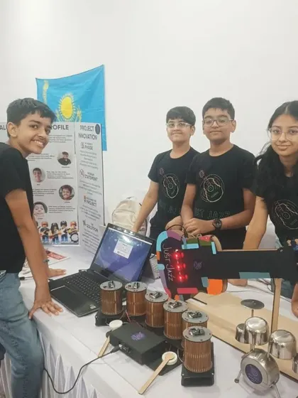 The 'Just Jazz' team proudly showcasing their automated musical instrument project at a competition. They built a robotic drum set and guitar that can be programmed to play tunes.
