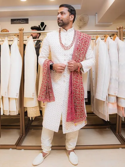 A client looking sharp in our white textured sherwani, paired perfectly with a contrasting red embroidered stole and a multi-layered necklace.